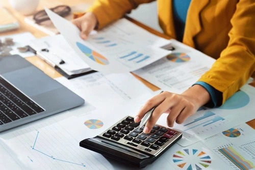 Person using a calculator while reviewing documents, illustrating how much a Dallas personal injury case may be worth.