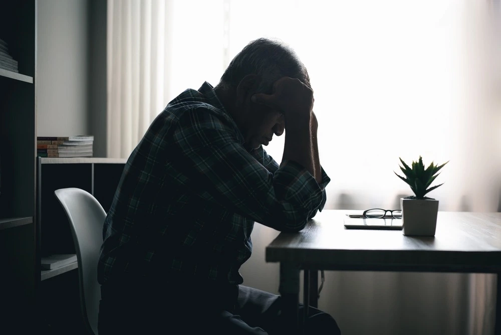 Tired person sitting in a dimly lit room, illustrating the symptoms and long-term effects of traumatic brain injuries.