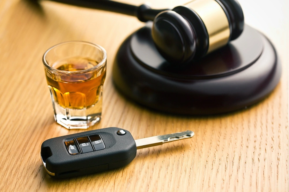 Car keys and an alcoholic drink placed beside a courtroom gavel, illustrating why drunk driving crashes are treated differently from other accidents under the law.