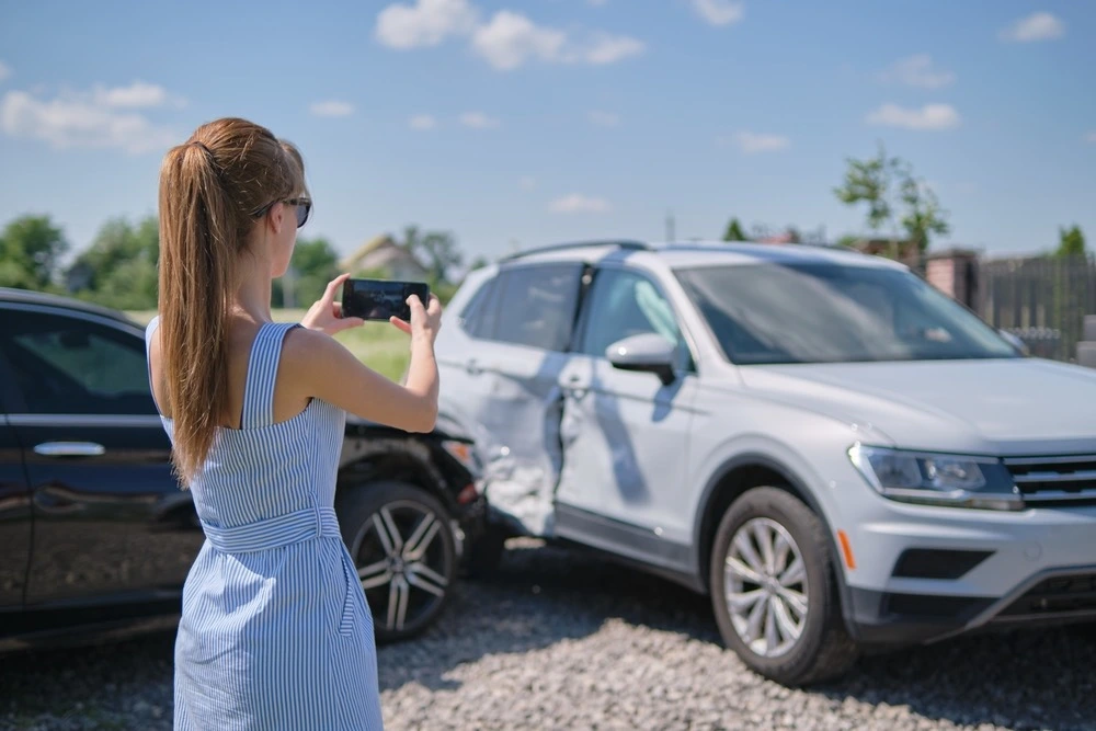 Person taking photos of a damaged vehicle at an accident scene, illustrating what to do after an accident in Rio Grande City.